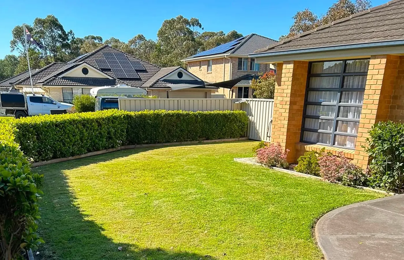 A corner lawn mown with the hedge line trimmed straight beside the house