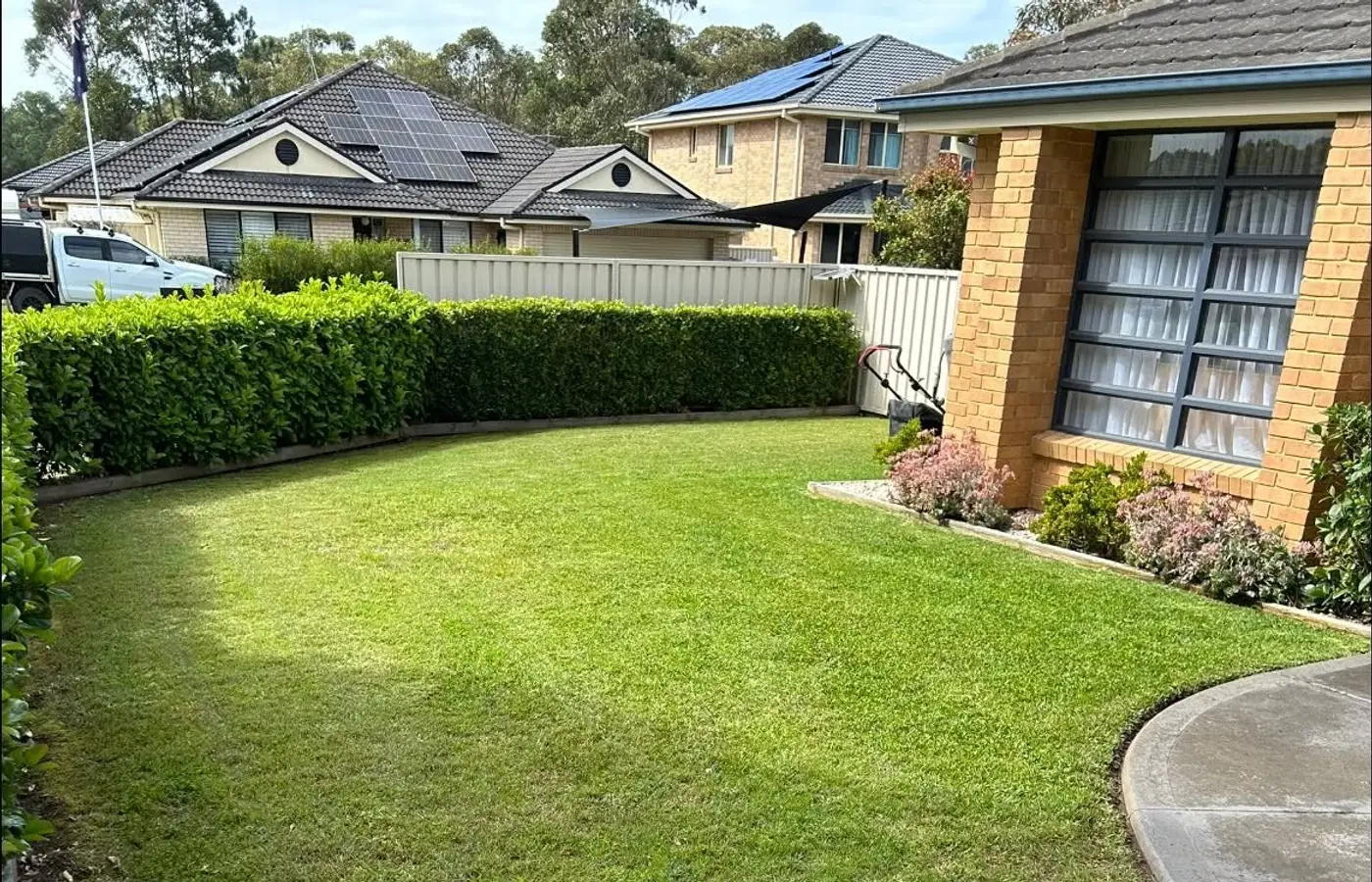 A neat green front lawn beside a brick home, mown and edged along the path